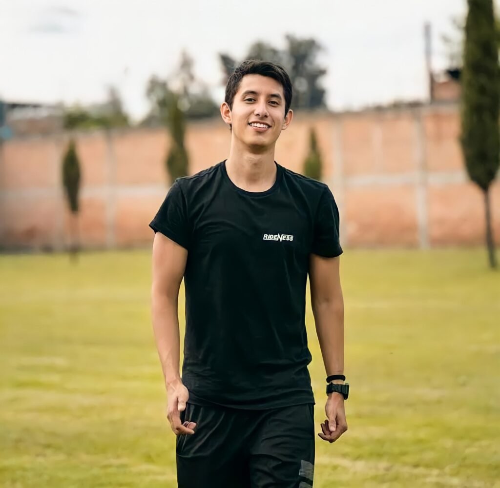 A young man in glasses writes in a notebook while sitting on a stylish couch indoors.